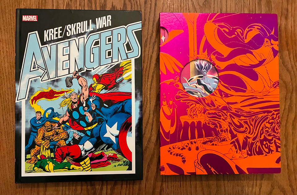 A photograph of two books sitting on my table. One is the oversized treasury edition hardcover collection of the classic Avengers storyline The Kree/Skrull War. The other is the luscious Beehive Books edition of The Blazing-World, in its bright purple and orange slipcase.