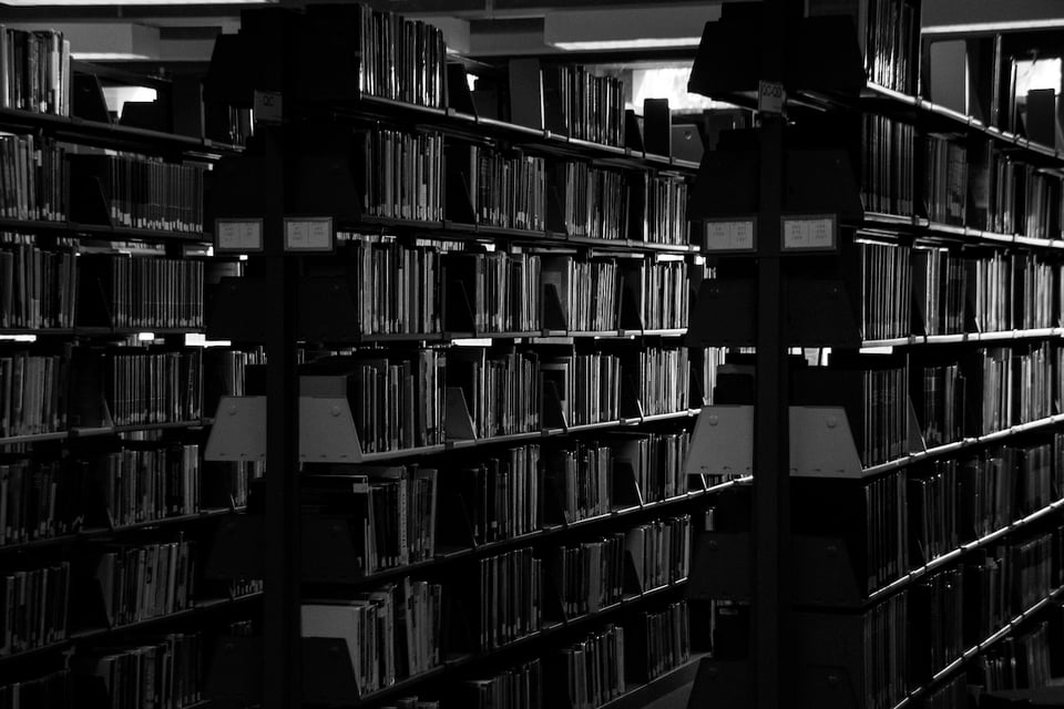 A black and white photo of library shelves in partial darkness