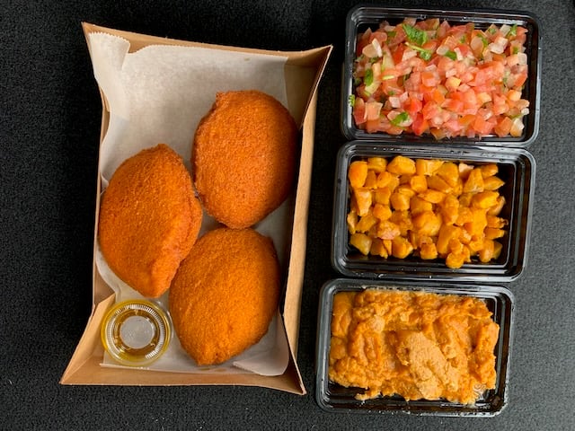 three dumplings sit in a paper box next to three containers of a paste, some chicken, and tomato salsa to stuff inside them