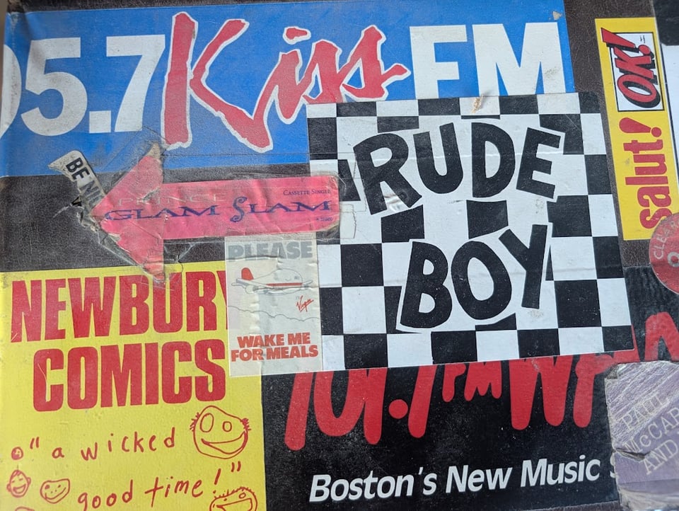 A box covered with stickers for radio stations, old albums, comic book shops, and other random junk