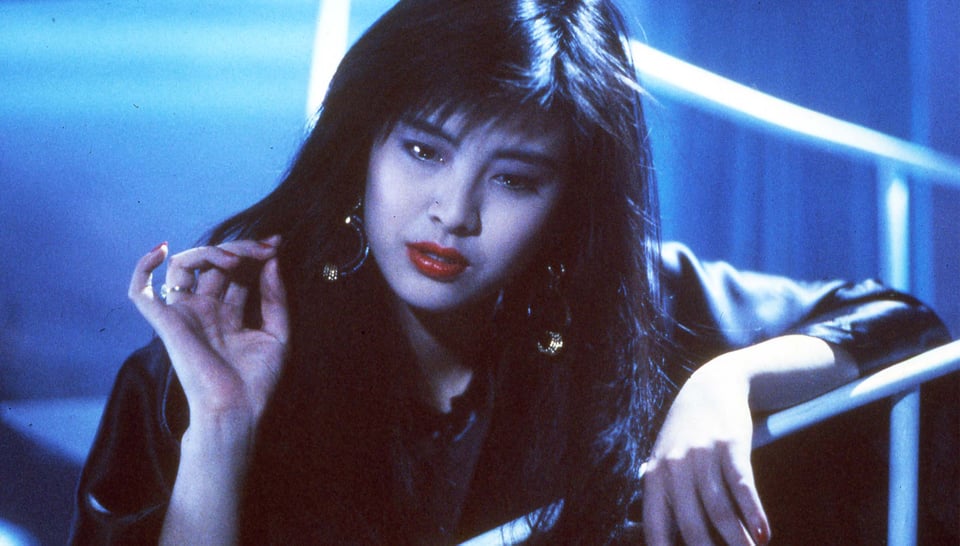 An Asian woman with long hair holds up one beautifully manicured hand, surrounded by glowy blue light. She's leaning on a railing