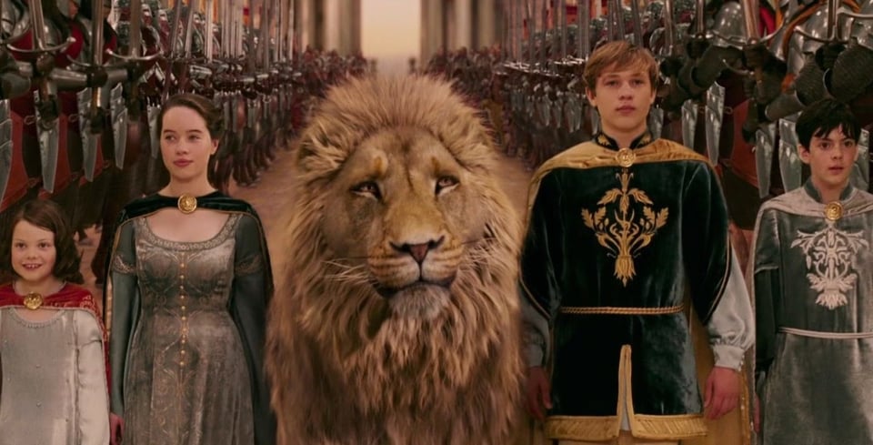 A group of kids in faux Medieval tunics and gowns with capes capes capes, with a lion at the center. A crowd is behind them.