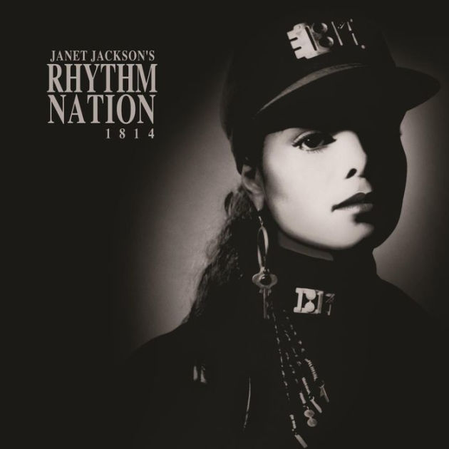 A black and white photo of Janet Jackson, a beautiful young Black woman, from the shoulders up. She wears a black cap, and a jacket with a military-style collar. The hat and the collar both have a metal plate that read 1814. She wears an a hoop earring with a key attached. She stares off to the right.