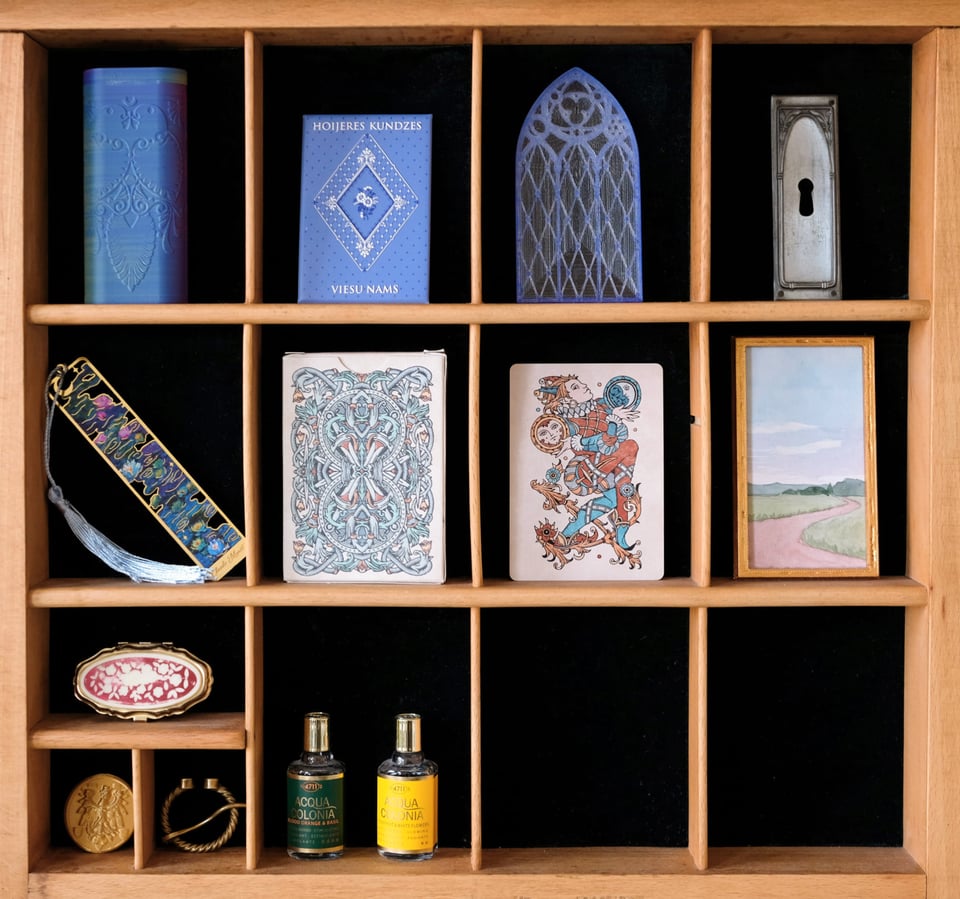 Photo close-up of the compartments and the trinkets inside. A bookmark, a playing card, a small watercolour landscape, a decorative keyhole and some perfume bottles, among other things.