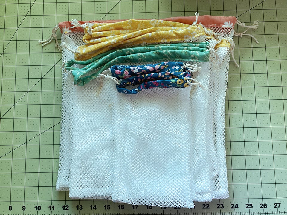 A stack of produce bags, each made with white mesh and a drawstring top made with varying colors of floral scrap fabric.