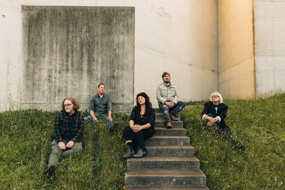 Four men and a woman sit on a slope featuring grass on either side of stairs descending from an angled concrete wall.
