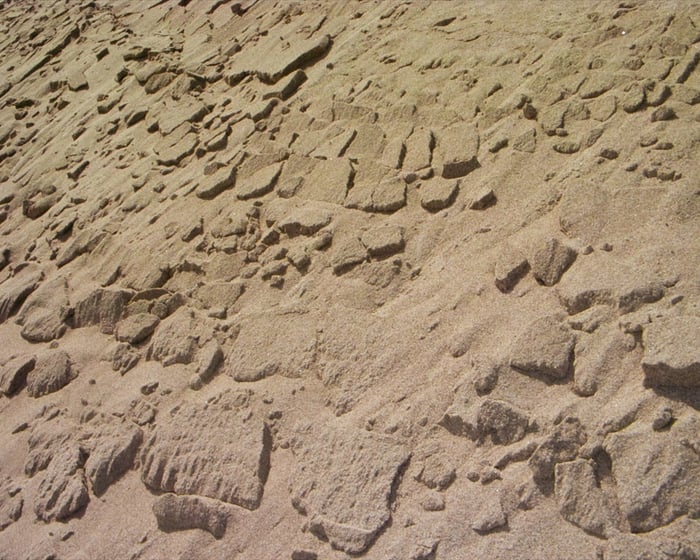 A slope of sand, the crust of it broken into shingles as it slowly slides down
