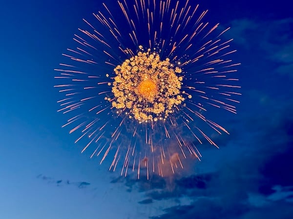 A large, bright orange firework explodes against a dark blue sky