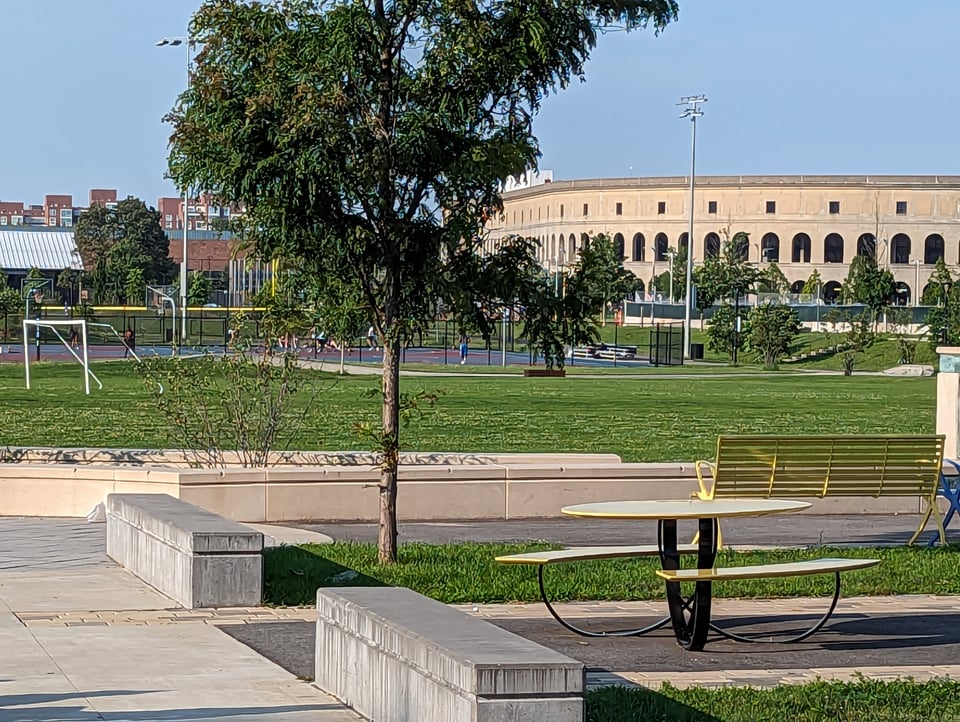 A city park with cement benches and a nice outdoor table, plus some sports fields and a colosseum