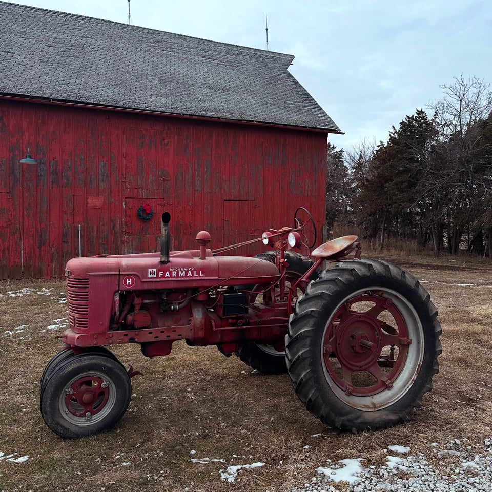 a red 1946 Farmall H tractor parked in front of a barn