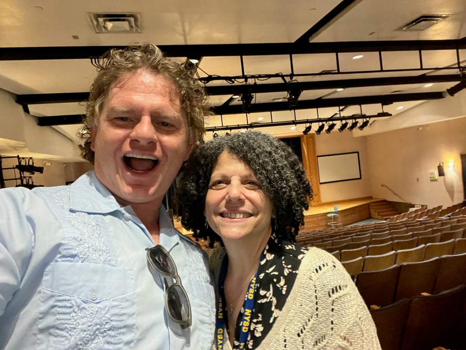 Two middle-aged white people, Will Fertman and Patti Marino-Aratingi, stand in front of an empty theater.