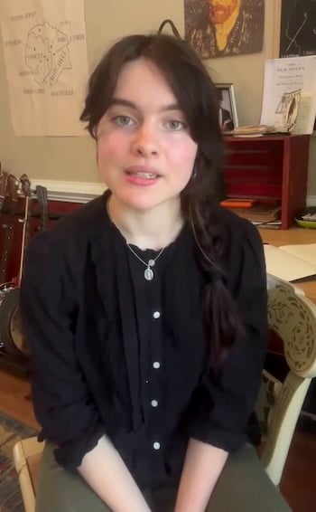 Murphy Campbell, seated, looks at the camera. Several stringed instruments (banjo etc.) are visible in the background.