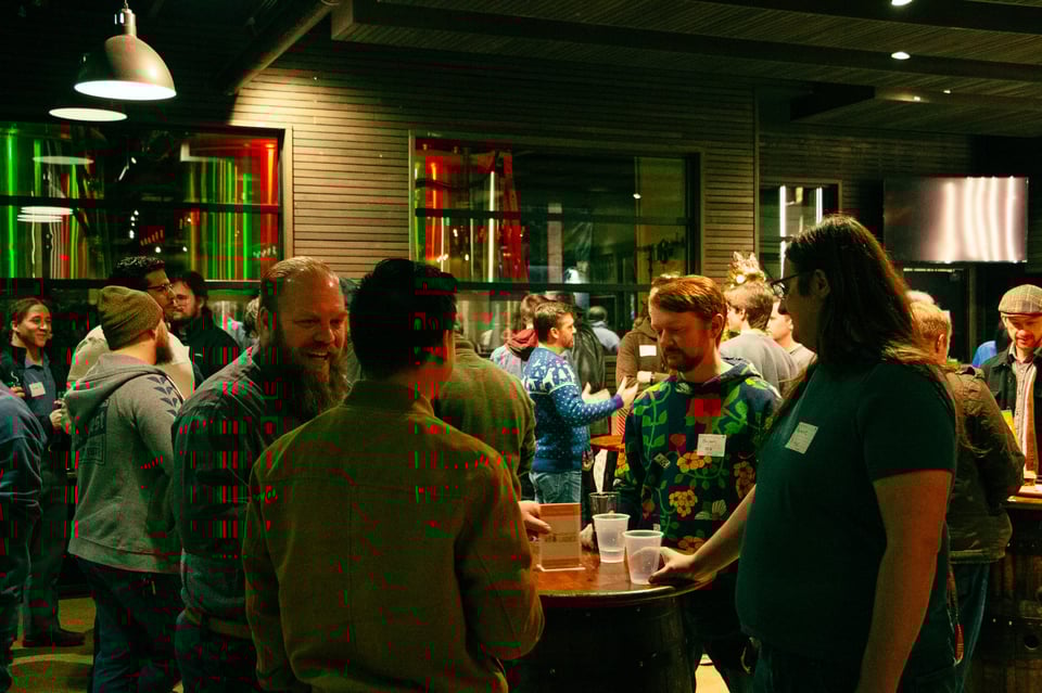 A group of people are gathered around small tables in a festive space at the 2024 Indy Hackers Holiday Social.