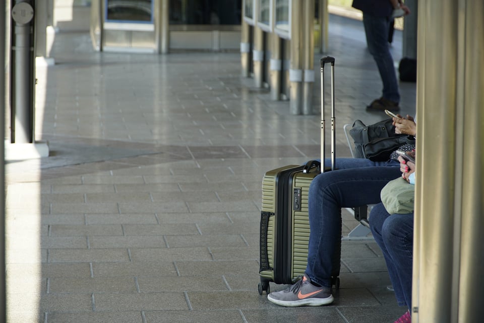 A couple looks at their phones while sitting in an airport, with their luggage.