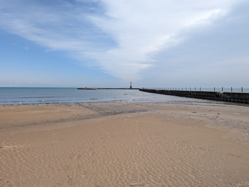 A long, narrow pier extending from a beach, with the tide out, and a big expansive sky with some high-up white clouds