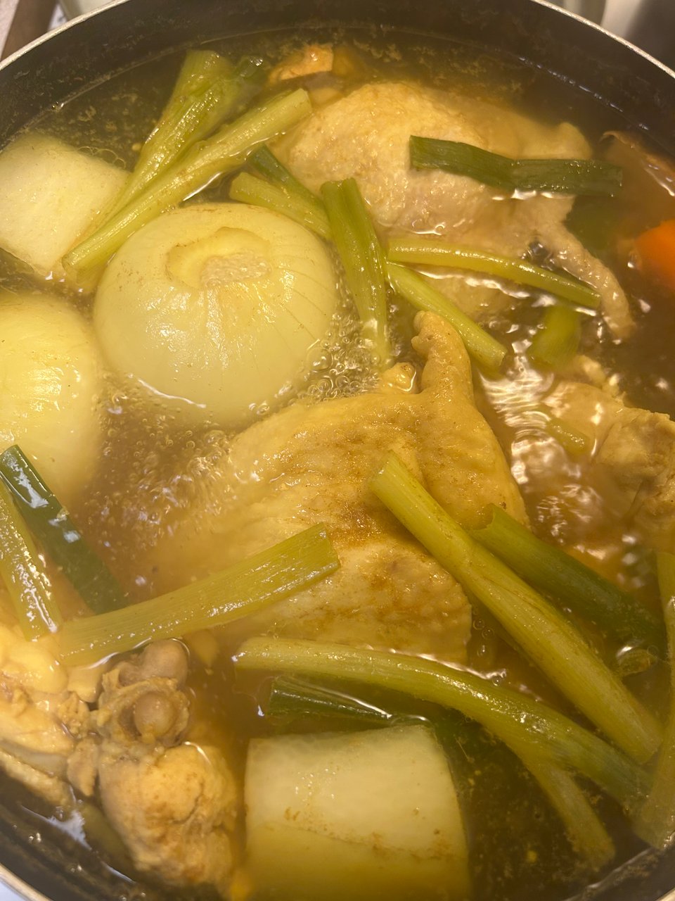 a photograph of a pot full of chicken broth, spring onions, and chicken thighs.