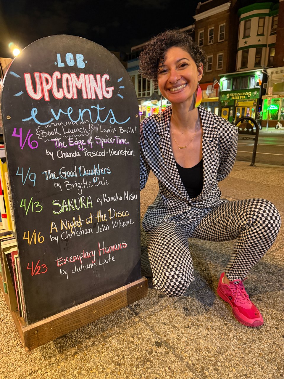 me next to the sign at Lost City Books announcing the events for the week. I'm wearing a catstooth suit and bright pink sneakers.