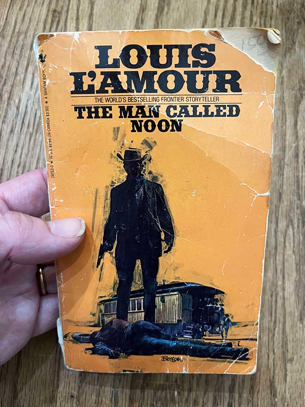 My hand holding a beat-up paperback book titled The Man Called Moon, featuring a man holding a gun on the cover.