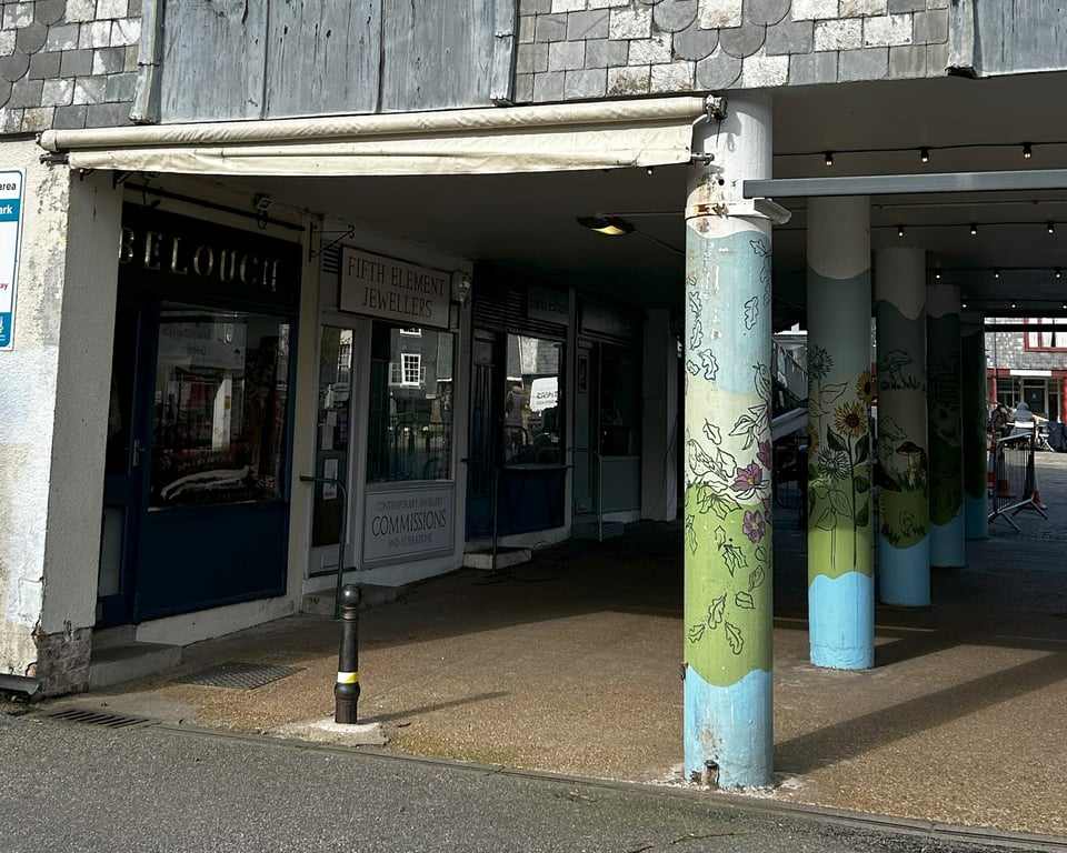 The small shops built into one of the end blocks of the Civic Hall, with a row of stilts in front of it. The stilts have been painted with waves of green and blue and stenciled with flowers.