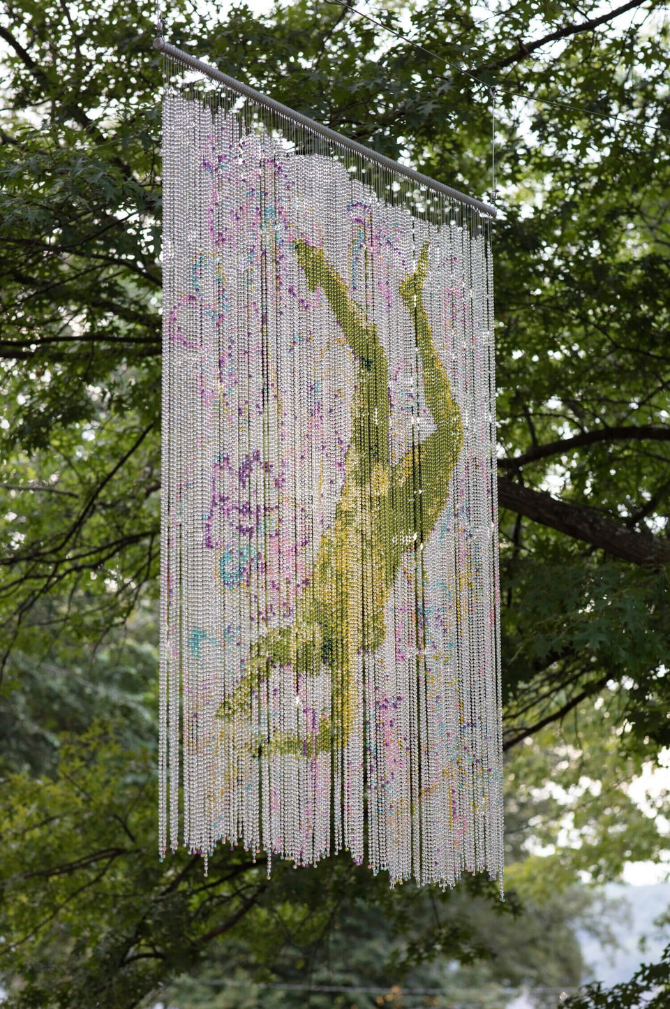 A beaded curtain with an image of a figure falling on it, hung in some trees.
