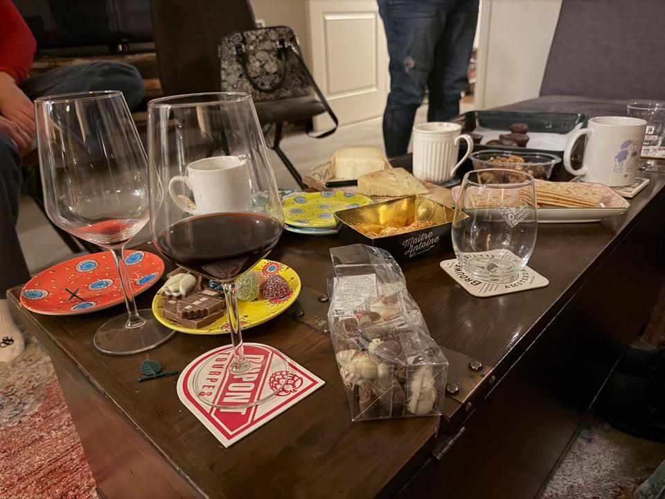 Coffee table filled with wine glasses, cups of tea, chocolate, cheese and crackers.