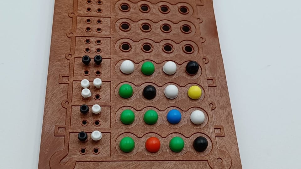 close up photo of a Mastermind board, with big coloiured pegs on the right and the smaller black-and-white pegs on the left