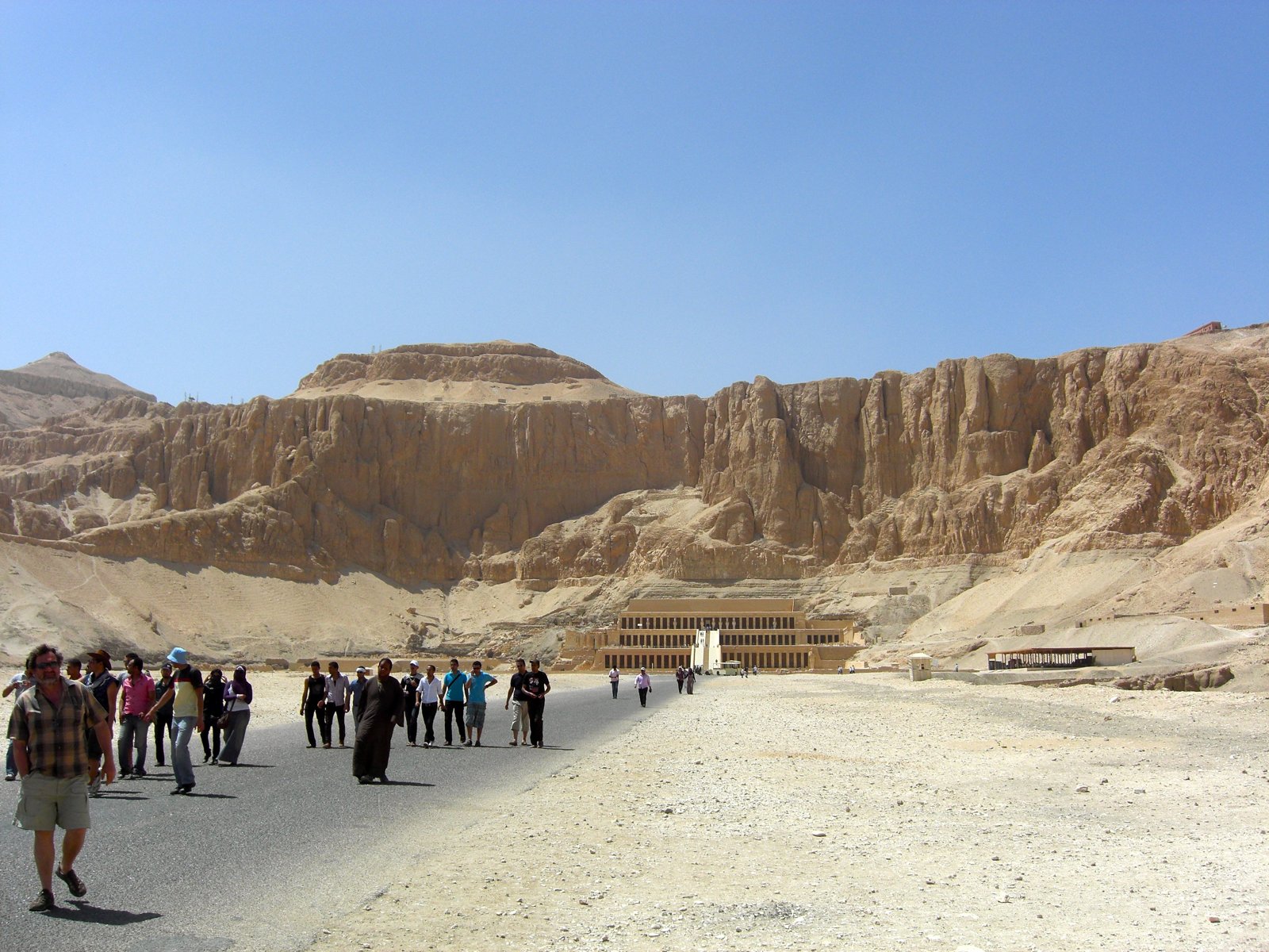 The mortuary temple of Hatshepsut carved into the cliff face at Deir el-Bahari, with tourists approaching on foot