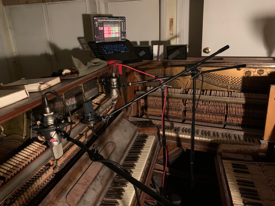 Several microphones arranged to record three ruined pianos placed in a tight booth.