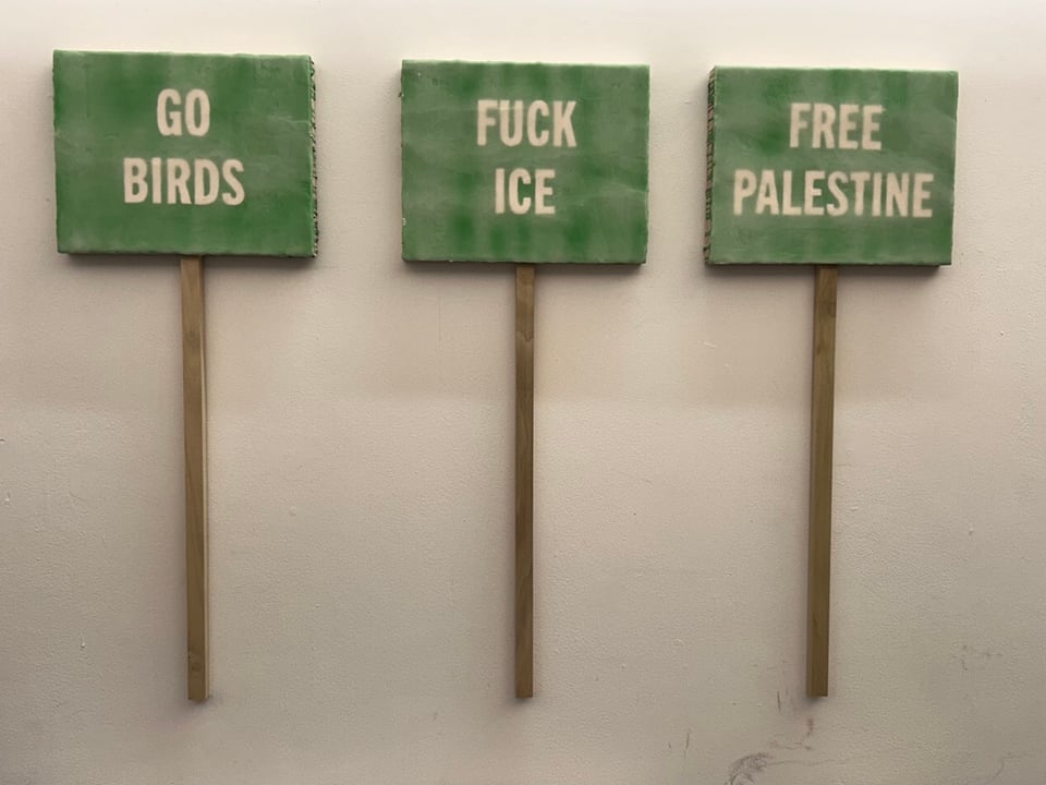 Three green paintings with sticks, to look like signs. White text. From L to R: GO BIRDS, FUCK ICE, FREE PALESTINE
