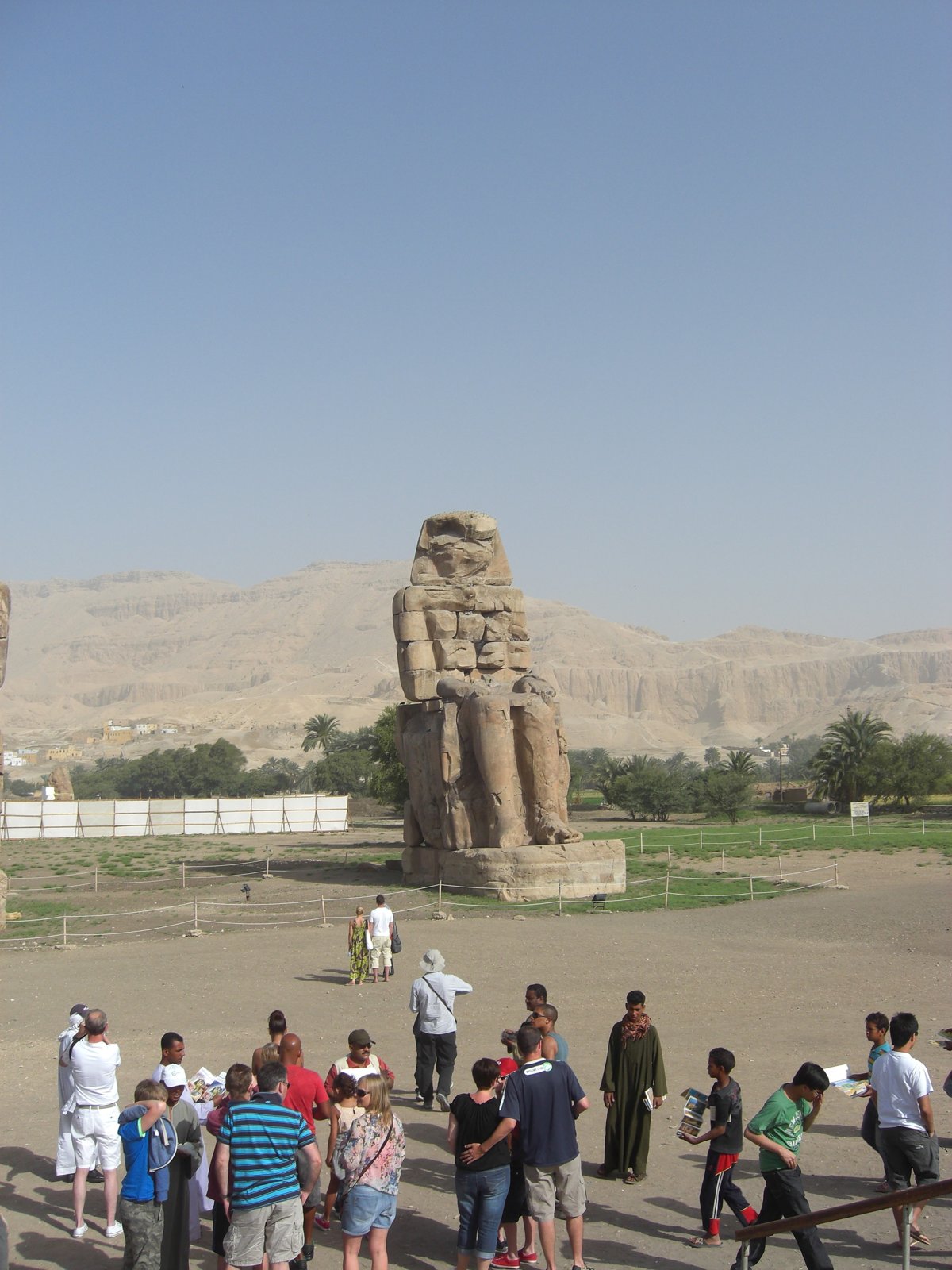 One of the Colossi of Memnon towering over tourists, with the Theban mountains in the background