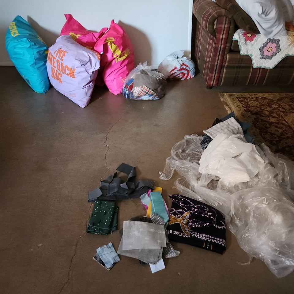 Photo of full bags of fabric on my living room floor, accompanied by empty trash bags and a few scraps.