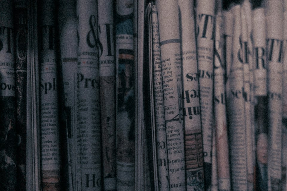 A person, seen from over their shoulder, reads a newspaper. Photo by Çağlar Oskay on Unsplash.