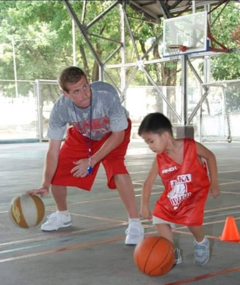 a white guy plays basketball with a little filipino kid in a red alaska jersey