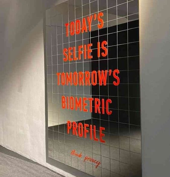 A full-length mirror has the following caption printed on it: "TODAY'S SELFIE IS TOMORROW'S BIOMETRIC PROFILE / think privacy"