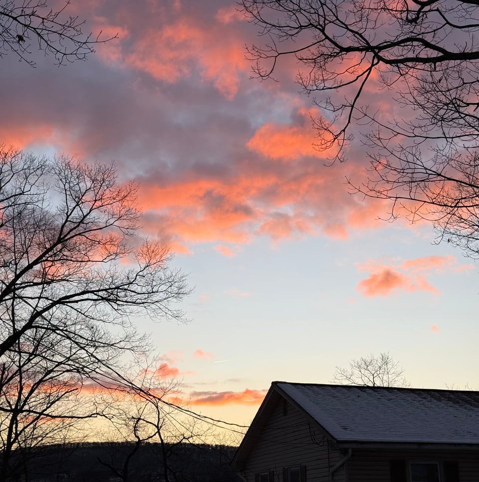 photo of sunrise, with the roof of a house in the foreground and hills in the background, with pink-gold-purple clouds above