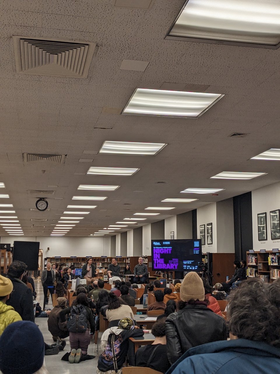 a group of people listening to a talk in a large library room.