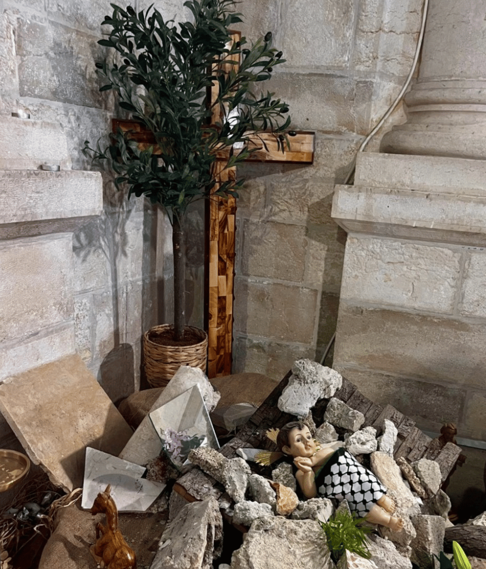 A cross and a doll lying atop concrete rubble, and wrapped in a black and white keffiyeh