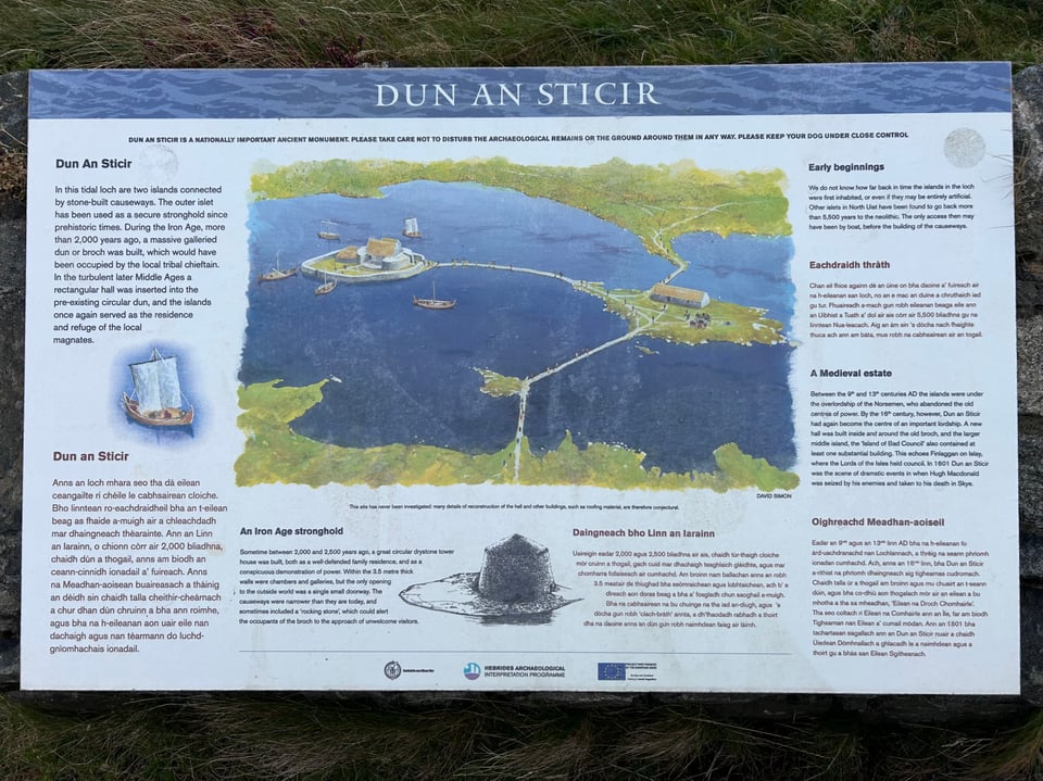An informational panel in Gaelic and English clearly showing Dun an Sticir in the Iron Age with three causeways connecting three islands to the shore with buildings constructed on two of the islands and boats gathering near the broch.