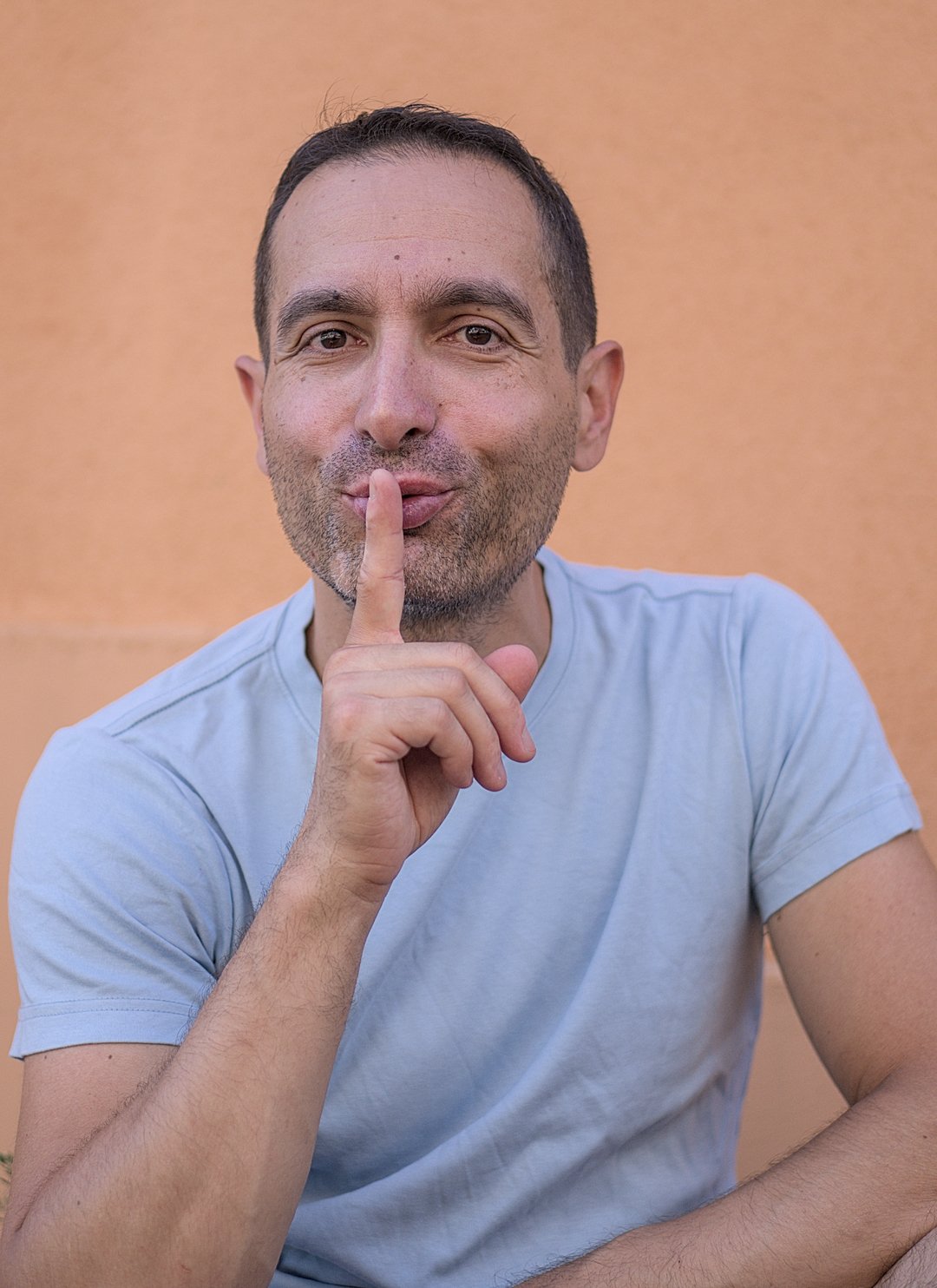 This is a portrait picture of me, Julien, smiling to the camera and putting my index finger in front of my mouth as if saying 'shush'