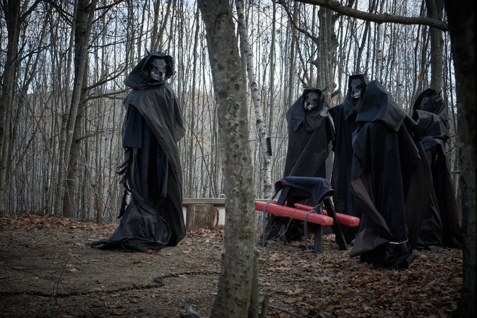a coven of figures in black robes in a fall forest
