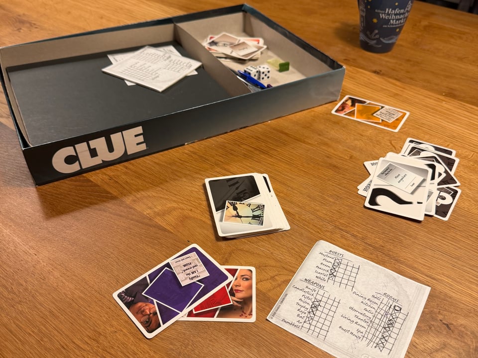 The board game Clue and the cards and score cards on a wooden dining room table after the game has finished.