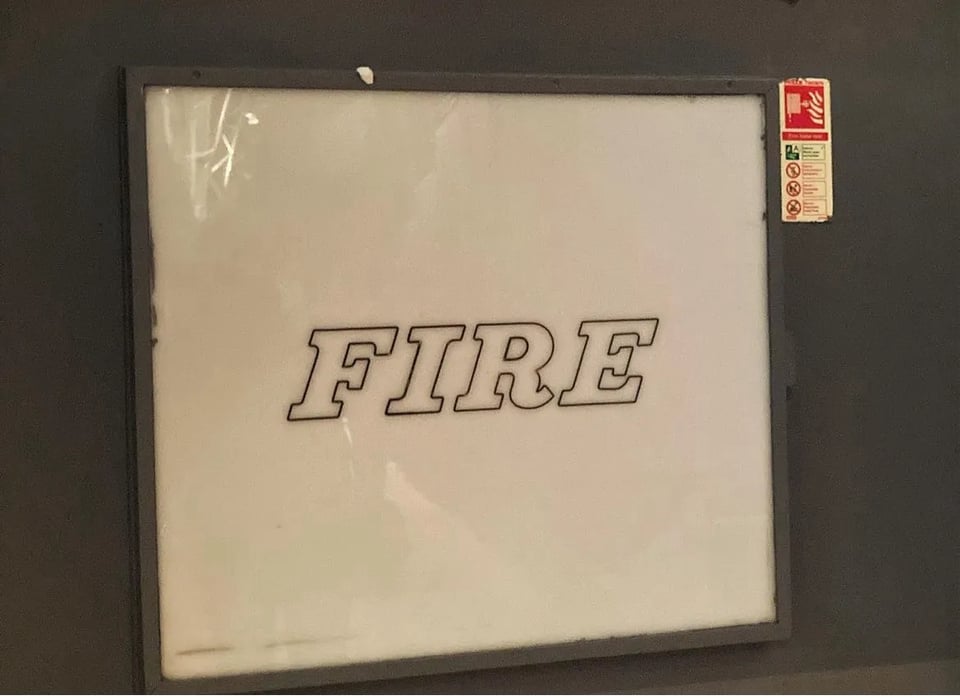 A large square white glass panel over an inset cupboard holding a fire hose. The word FIRE is in the centre in an outline festive-like font.