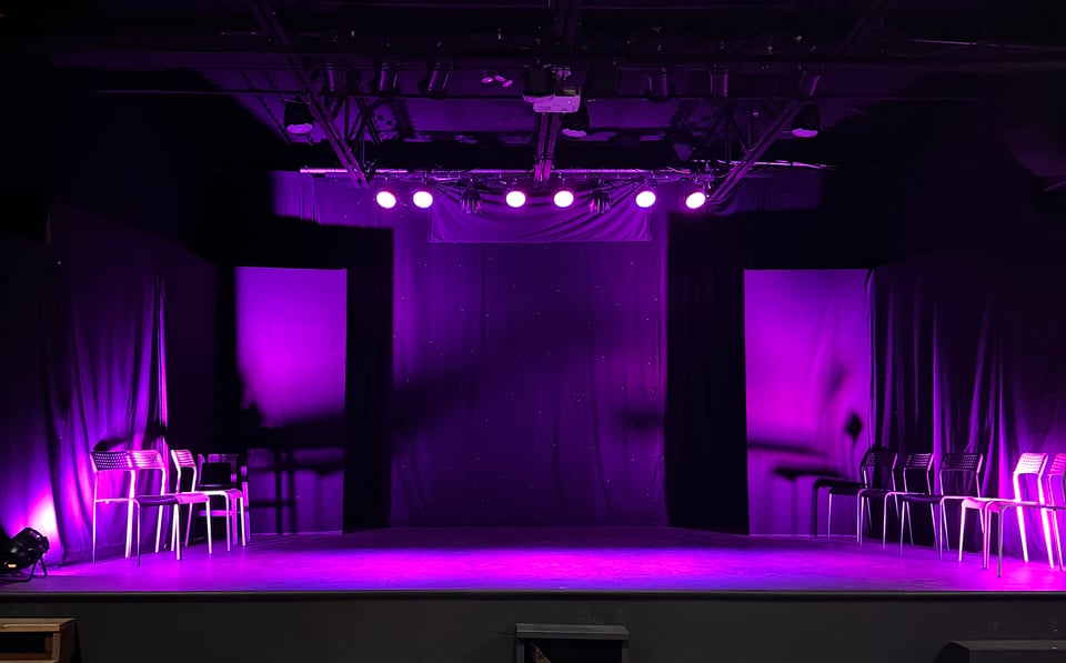An empty theatre stage is lit purple.