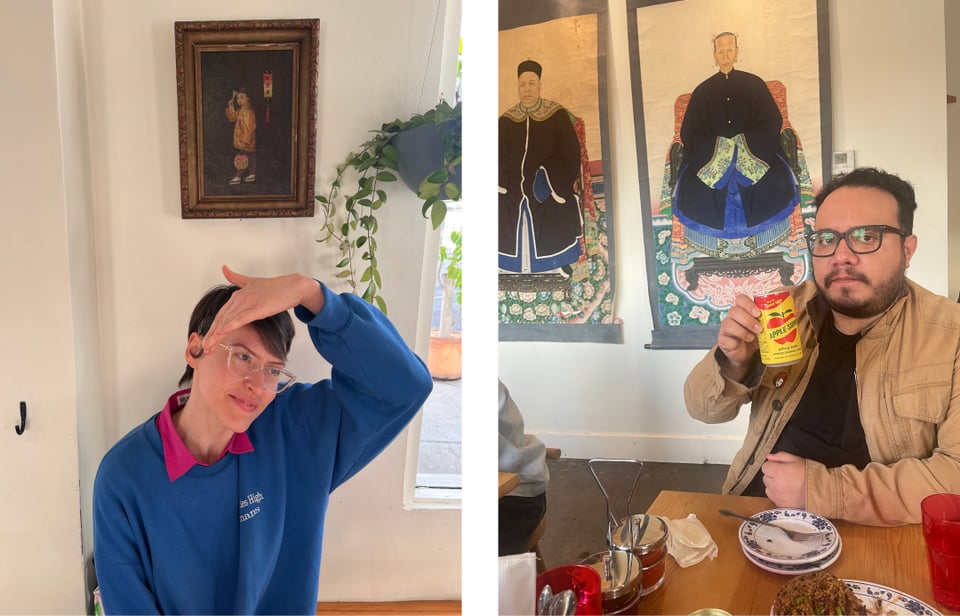 woman in blue sitting infront of a painting. man in tan jacket sitting infront of empty plates and two paintings.