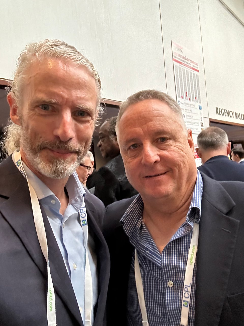 Photo of 2 white men in their 50s & 60s in navy suits and blue shirts at a trade show
