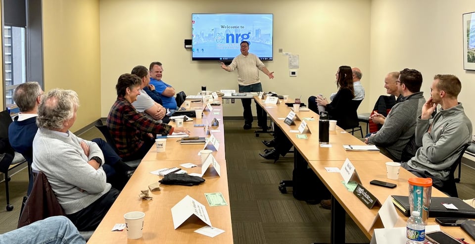 Paul poses with his arms reaching out in front of seated NRG members.