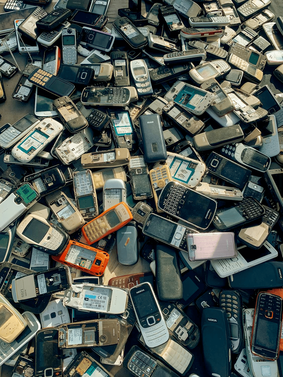 A photo of a massive pile of old dusty and broken mobile phones from the early 2000s.