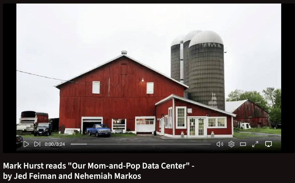 A red barn with two silos and an adjoining building, and trucks parked out front.