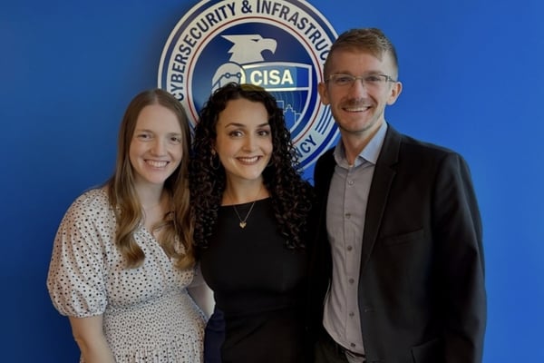 Three people pose together in front of a Cybersecurity and Infrastructure Security Agency, or CISA, backdrop.