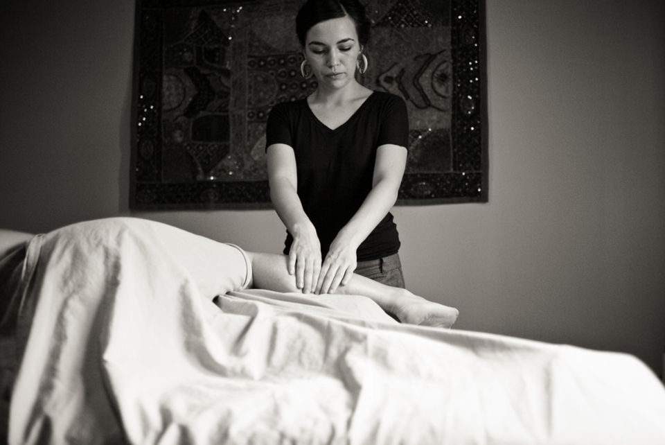 Black and white photo of a woman massaging a client's leg in her studio
